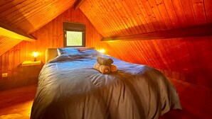A cozy attic bedroom with a sloped wooden ceiling, a bed with blue bedding, and a window with a view. - The Campagnarde (Flers)