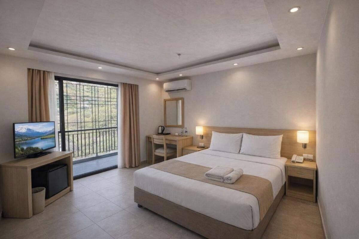 A hotel room with a bed, bedside tables, a desk, a TV, and a window with curtains.