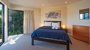 Une chambre à coucher avec un grand lit, une table de chevet, une commode, une fenêtre avec des rideaux et un tableau au mur.