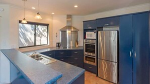Une cuisine moderne dotée d’appareils électroménagers en acier inoxydable, d’une grande fenêtre et de meubles de couleur bleue.