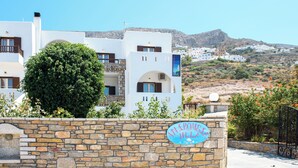 Muro de piedra con un letrero que dice 'ATLAPOMVILLA' y un edificio moderno con balcones y montañas al fondo.
