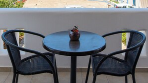 Un balcón con dos sillas y una mesa, con vistas a una colina con edificios.