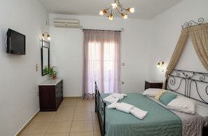 Une chambre à coucher comprenant un lit, un téléviseur, une commode, un miroir, une fenêtre avec des rideaux et un luminaire au plafond.