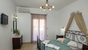 Un dormitorio con cama, mesita de noche, televisor, espejo, ventana con cortinas y lámpara en el techo.