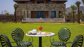 A modern house with a stone facade, a pool, and a dining area with chairs and a table set for a meal. - ELIVAAS The Kanota Retreat 4 BHK Villa (Jaipur)