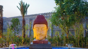 A Buddha statue in a pool with a stone wall and palm trees in the background. - ELIVAAS The Kanota Retreat 4 BHK Villa (Jaipur)