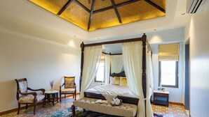 A bedroom with a four-poster bed, a bench, two chairs, a small table, and a patterned carpet. - ELIVAAS The Kanota Retreat 4 BHK Villa (Jaipur)