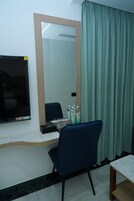 A hotel room with a desk, a chair, a mirror, a television, and a curtain.