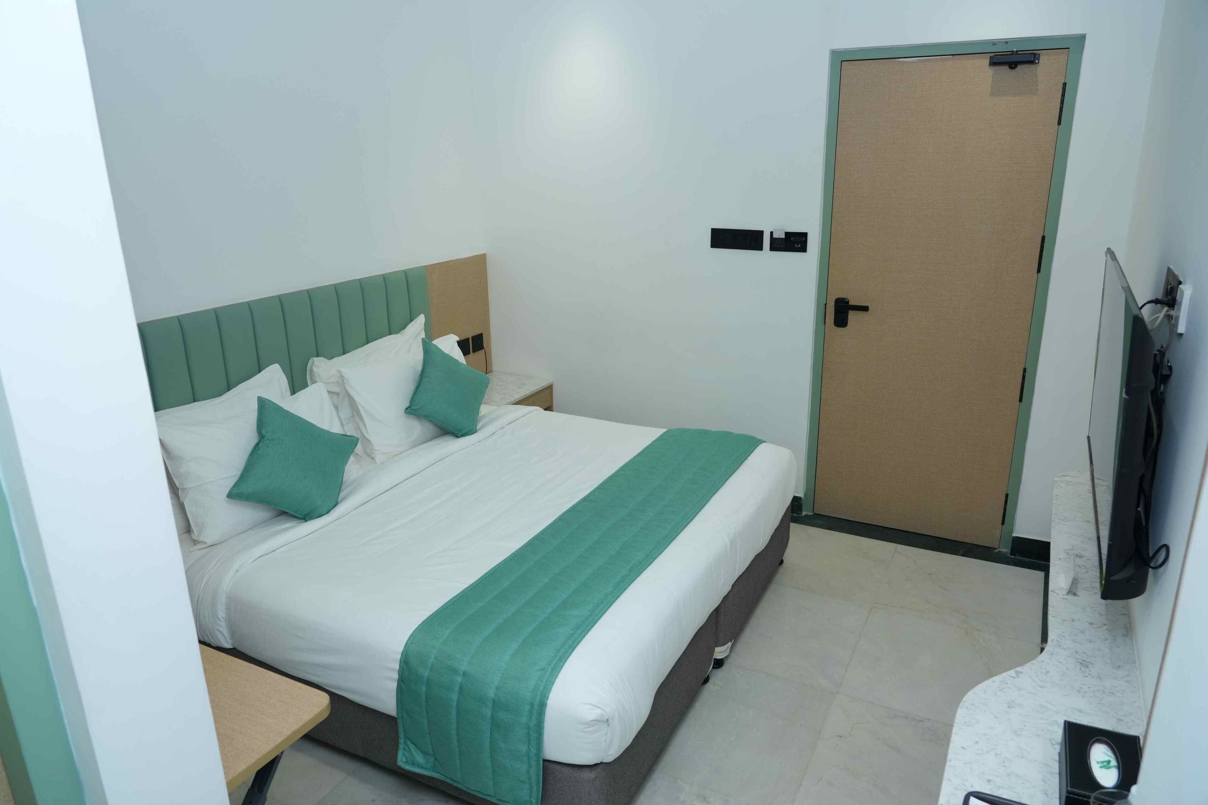 Habitación de hotel con cama, mesita de noche, televisor y puerta.