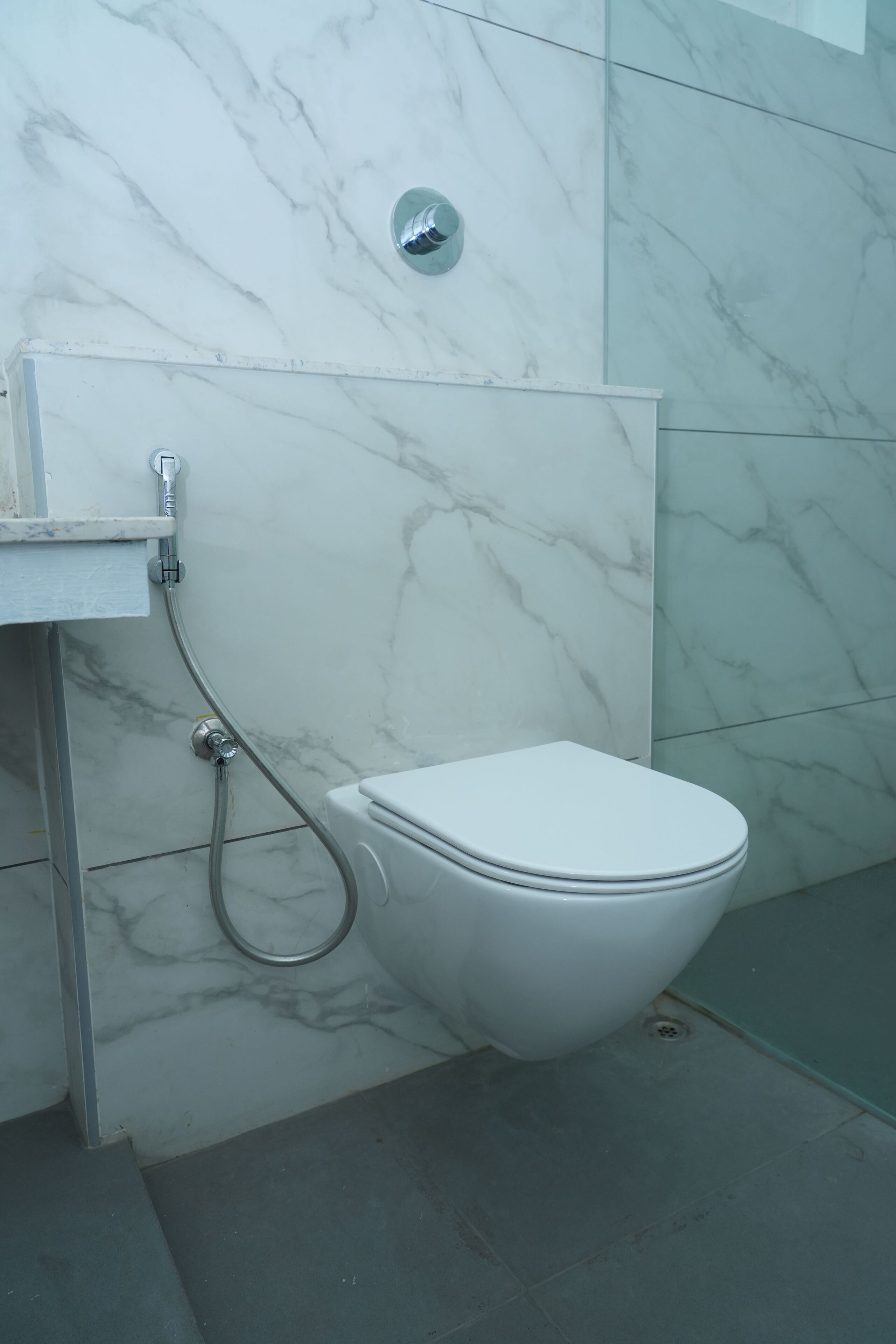 Baño con inodoro blanco, ducha y pared de mármol.