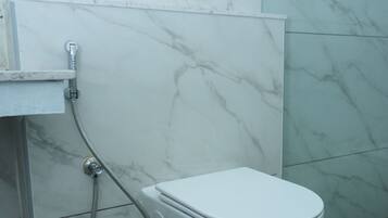 Baño con inodoro blanco, ducha y pared de mármol.