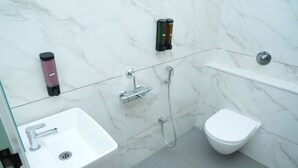 Une salle de bain moderne avec un lavabo blanc, un bidet, un distributeur de savon à main et une douchette à main.