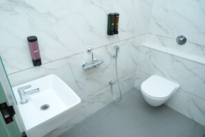 A modern bathroom with a white sink, a bidet, a handheld soap dispenser, and a handheld showerhead. - Hotel Niyathi (Erode)