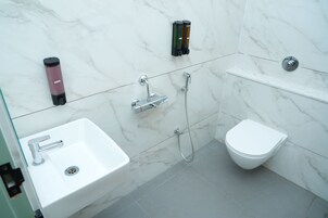 A modern bathroom with a white sink, a bidet, a handheld soap dispenser, and a handheld showerhead.