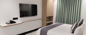 Une chambre d’hôtel équipée d’un lit, d’un téléviseur à écran plat fixé au mur, d’une machine à café et d’une fenêtre avec des rideaux.
