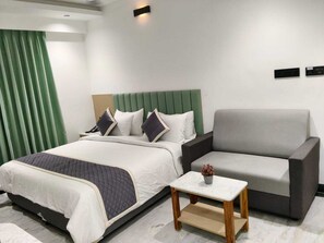 Une chambre d’hôtel moderne avec un lit, un fauteuil gris, une petite table et un rideau vert.