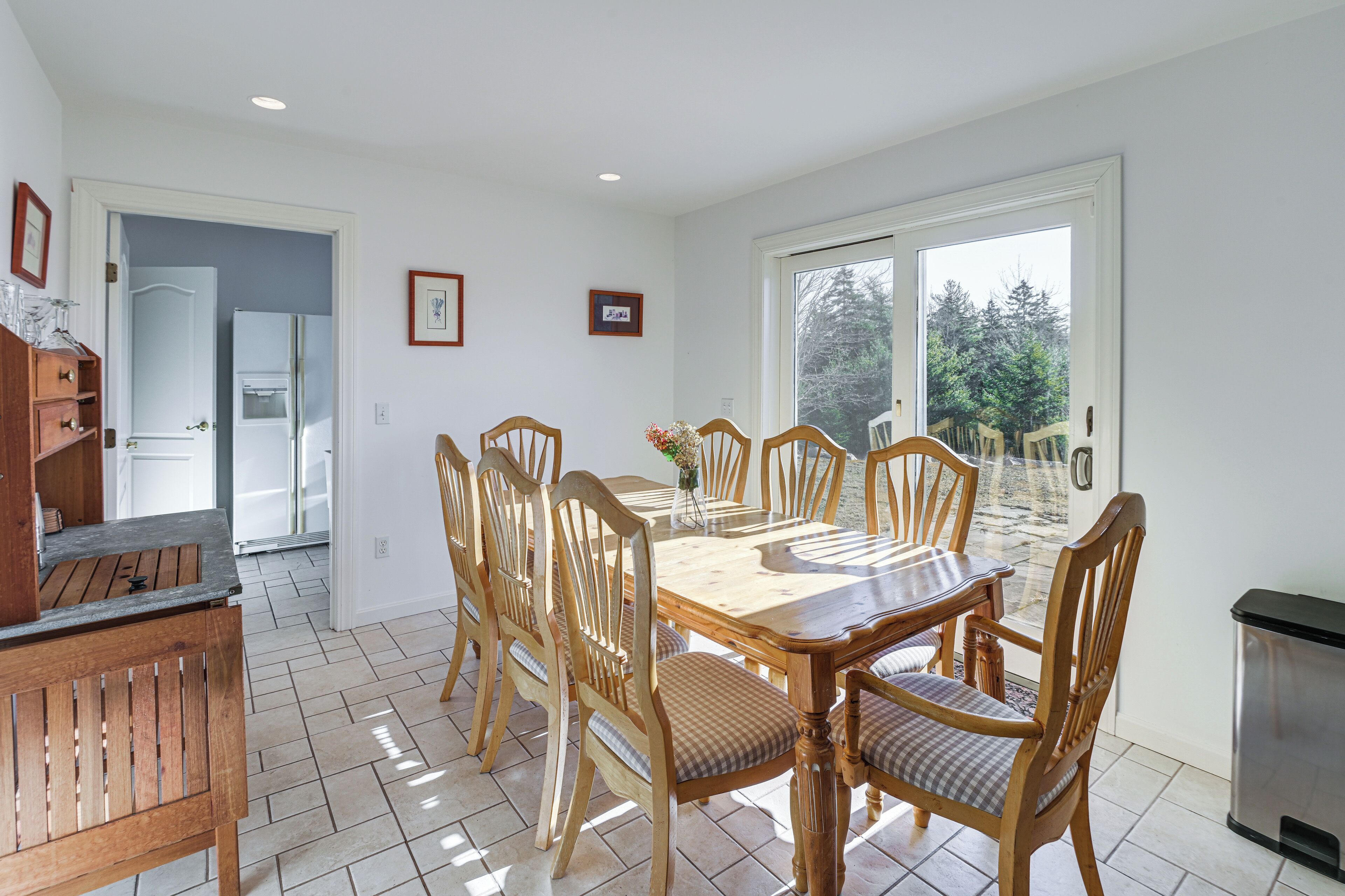 A dining area with a wooden table and chairs, a kitchen area with a refrigerator, and a view through a glass door.