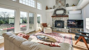 A spacious living room with a stone fireplace, a television, and a large window overlooking a garden. - Sweetmoss Is Lovely! 3 Mi to Acadia Nat'l Park (Mount Desert)
