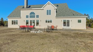 A two-story house with a chimney, large windows, and a covered patio area with outdoor furniture. - Sweetmoss Is Lovely! 3 Mi to Acadia Nat'l Park (Mount Desert)