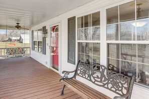 Eine Veranda mit Holzbank, großen Fenstern und Deckenventilator.
