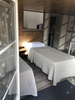 A bedroom with two beds, a wooden headboard, a bedside table with a lamp, and a mirror above the bed. - Large 22 m2 ground-floor studio, 5-minute walk from IGR/Paul Brousse line 14 (Villejuif)