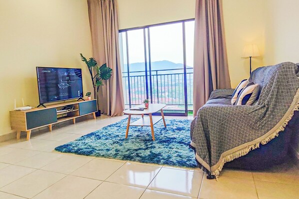 A living room with a TV, sofa, coffee table, and a view of the outdoors. - Warm Nest at Youth City Nilai by HCK (Nilai)