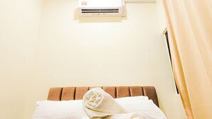 A hotel room with a bed, a pillow, a rolled towel, an air conditioner, and a window with curtains.