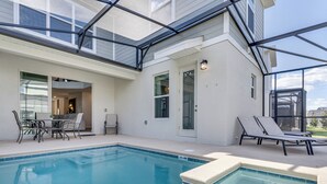 Ein Schwimmbecken mit Glasabdeckung, eine Terrassenfläche mit Stühlen und Tisch sowie eine Tür zu einem Innenbereich.