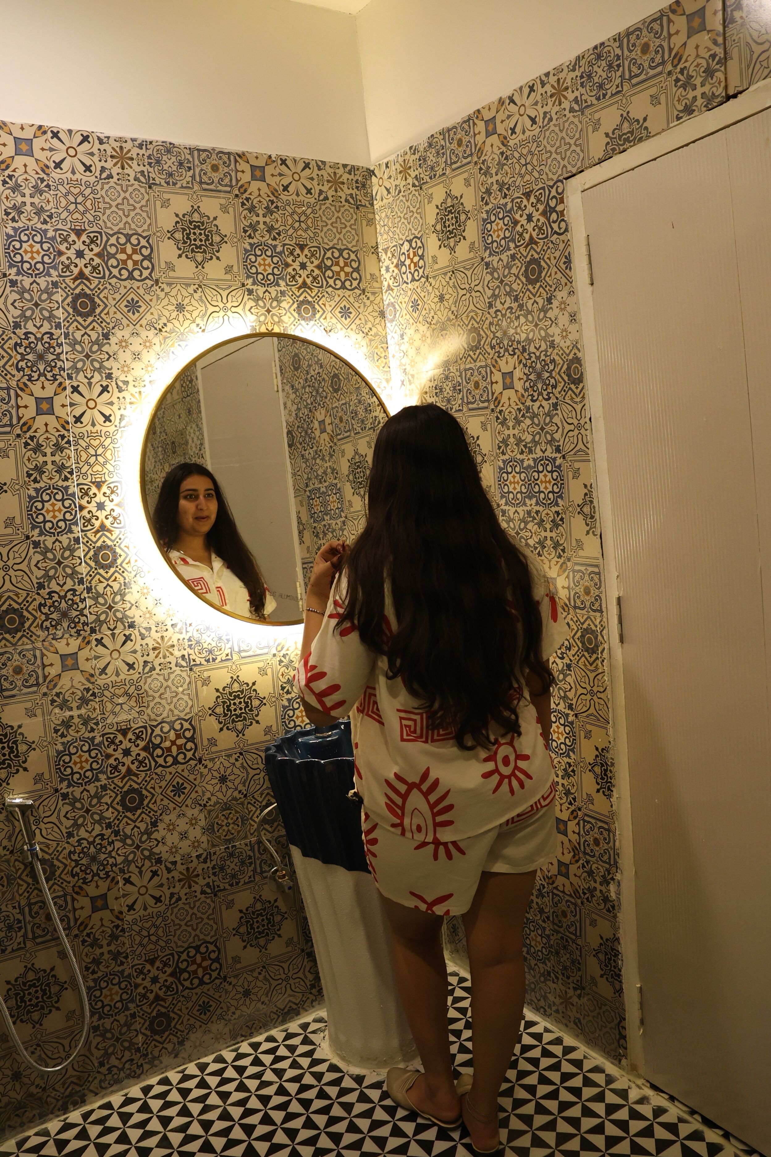 Une salle de bain avec des carreaux décorés, un miroir rond et une douche.