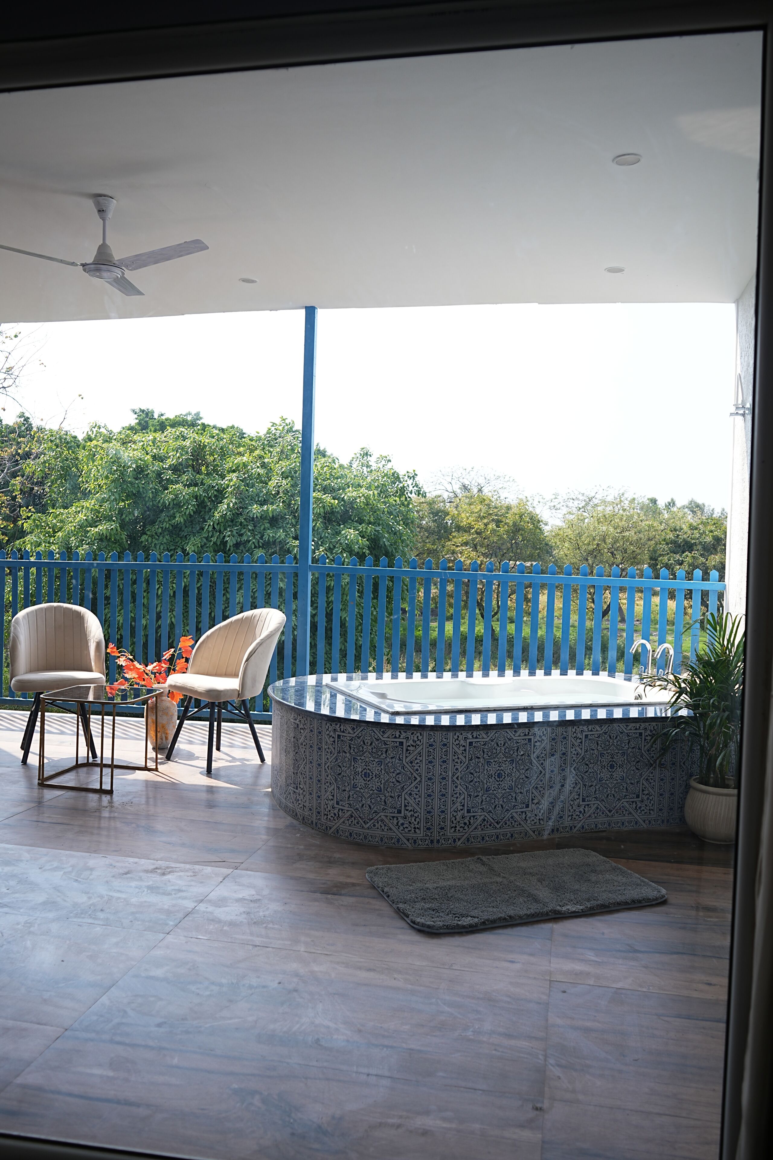 A patio with a round table, two chairs, a blue fence, and a ceiling fan.