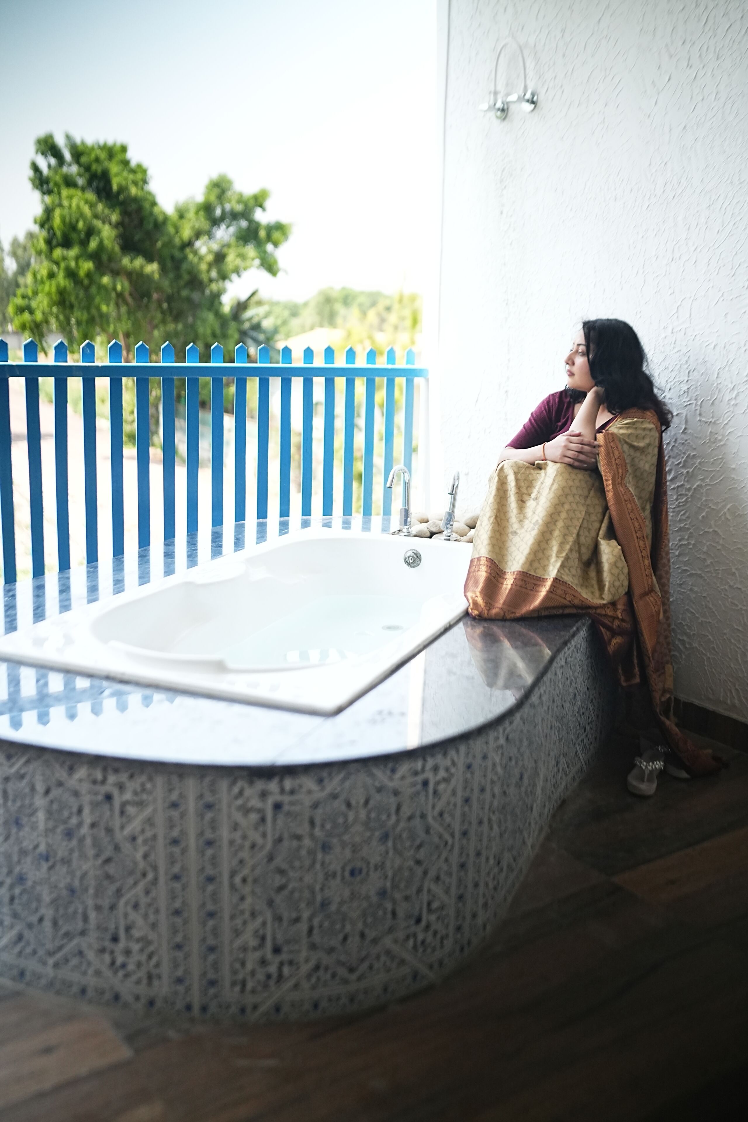 A person sitting by a bathtub with a blue fence in the background.