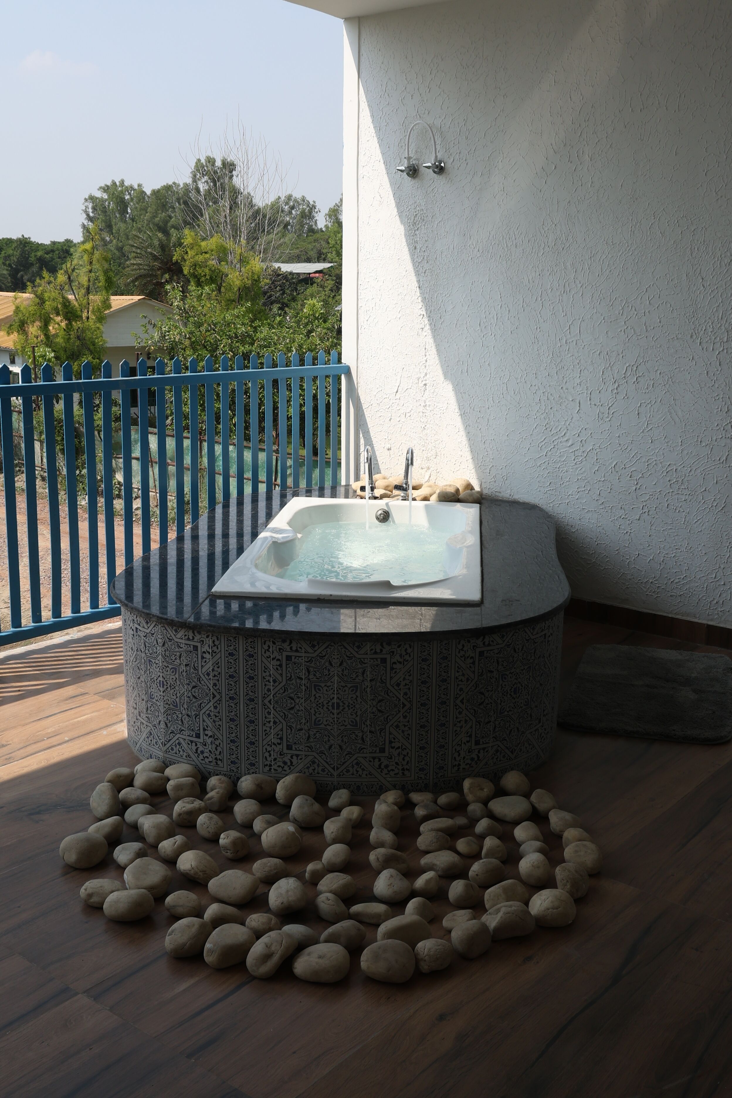 A hot tub with a patterned surround, a stone arrangement, and a blue fence.