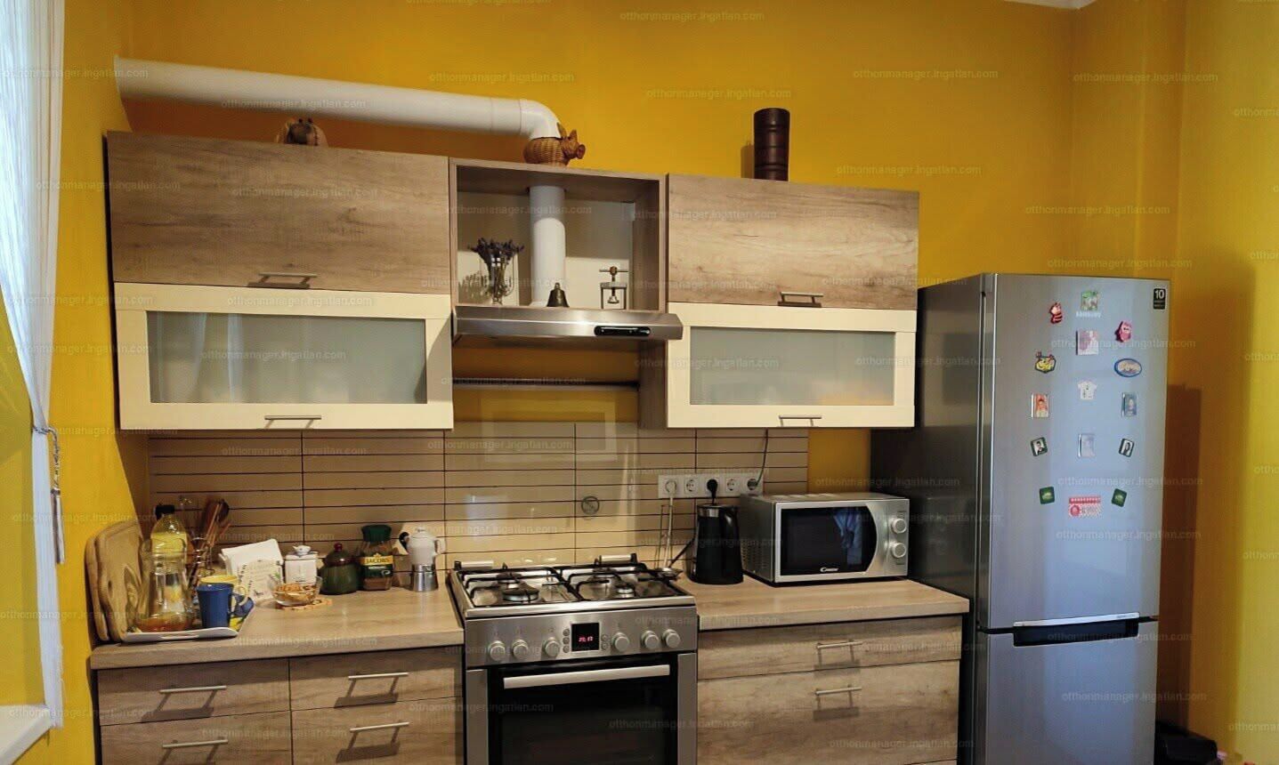 Een keuken met houten kastjes, een gasfornuis, een magnetron en een koelkast.
