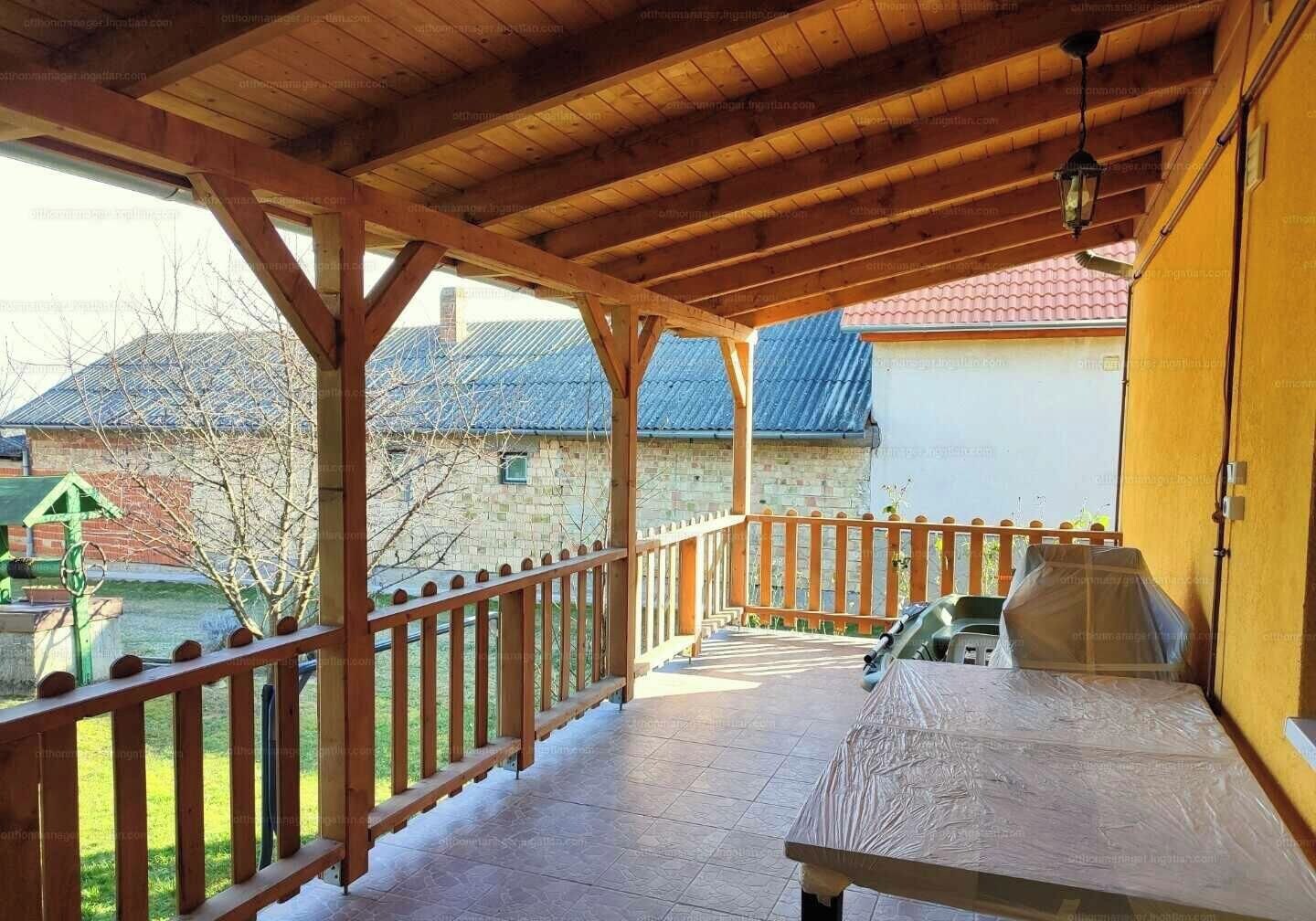 A covered outdoor area with a wooden deck, a table, and a view of a house with a red roof.