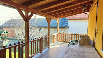 A covered outdoor area with a wooden deck, a table, and a view of a house with a red roof.