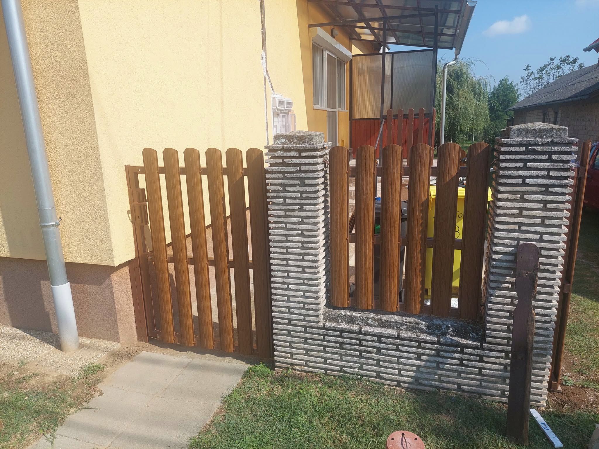 A gated entrance with a wooden fence and stone pillars.
