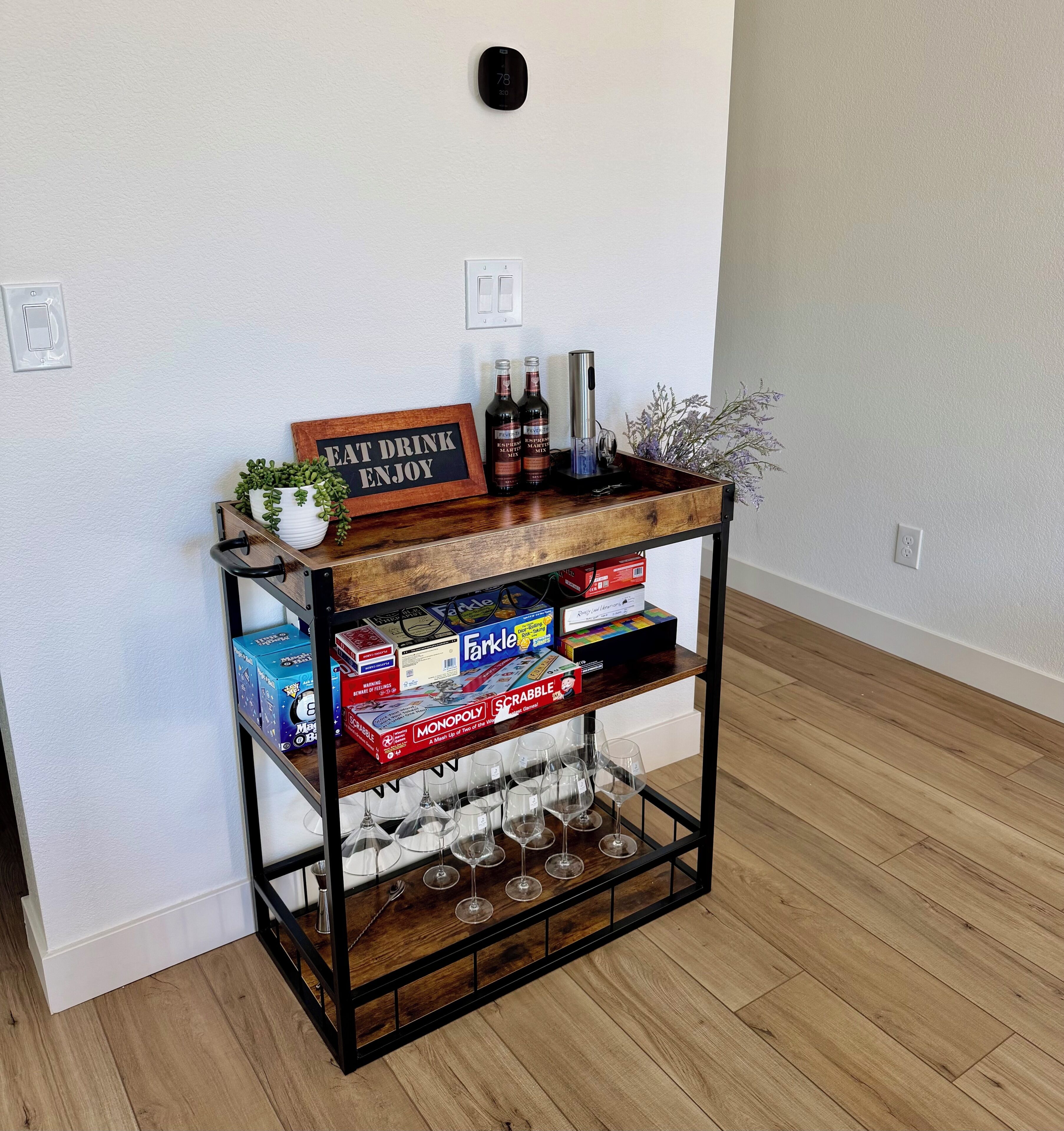 A wooden console table with a sign that reads 'EAT DRINK ENJOY' and two bottles of wine.