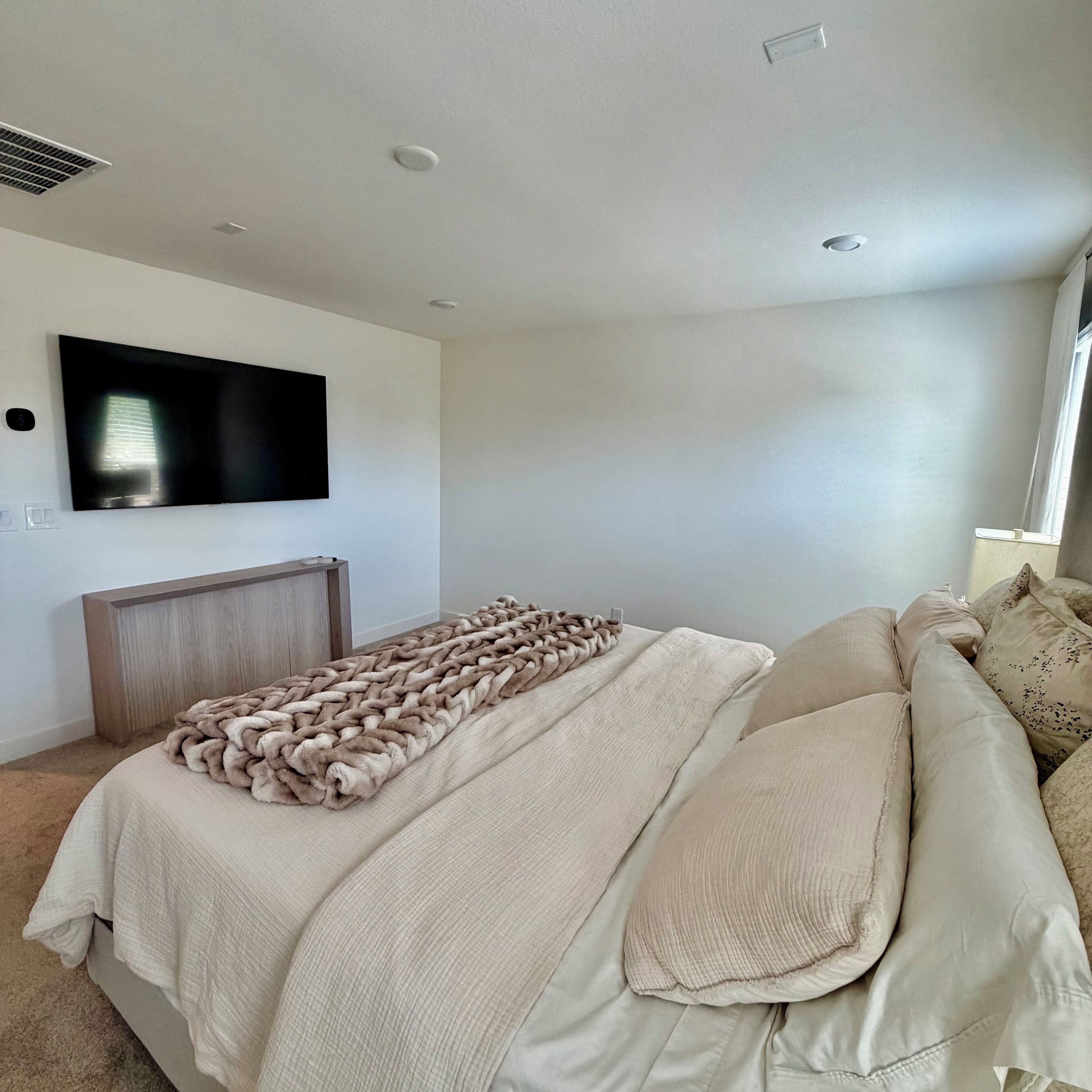 A bedroom with a bed, a TV mounted on the wall, a window, and a radiator.