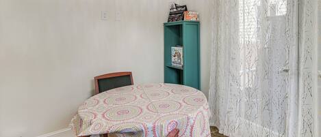 A small room with a bed, a chair, a teal bookshelf, and a window with sheer curtains.