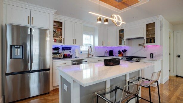 Een moderne keuken met witte kasten, roestvrijstalen apparatuur en een centraal eiland met barkrukken.