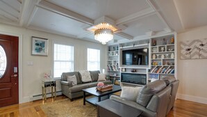 Een woonkamer met een kroonluchter, een open haard, een boekenkast en een bank.