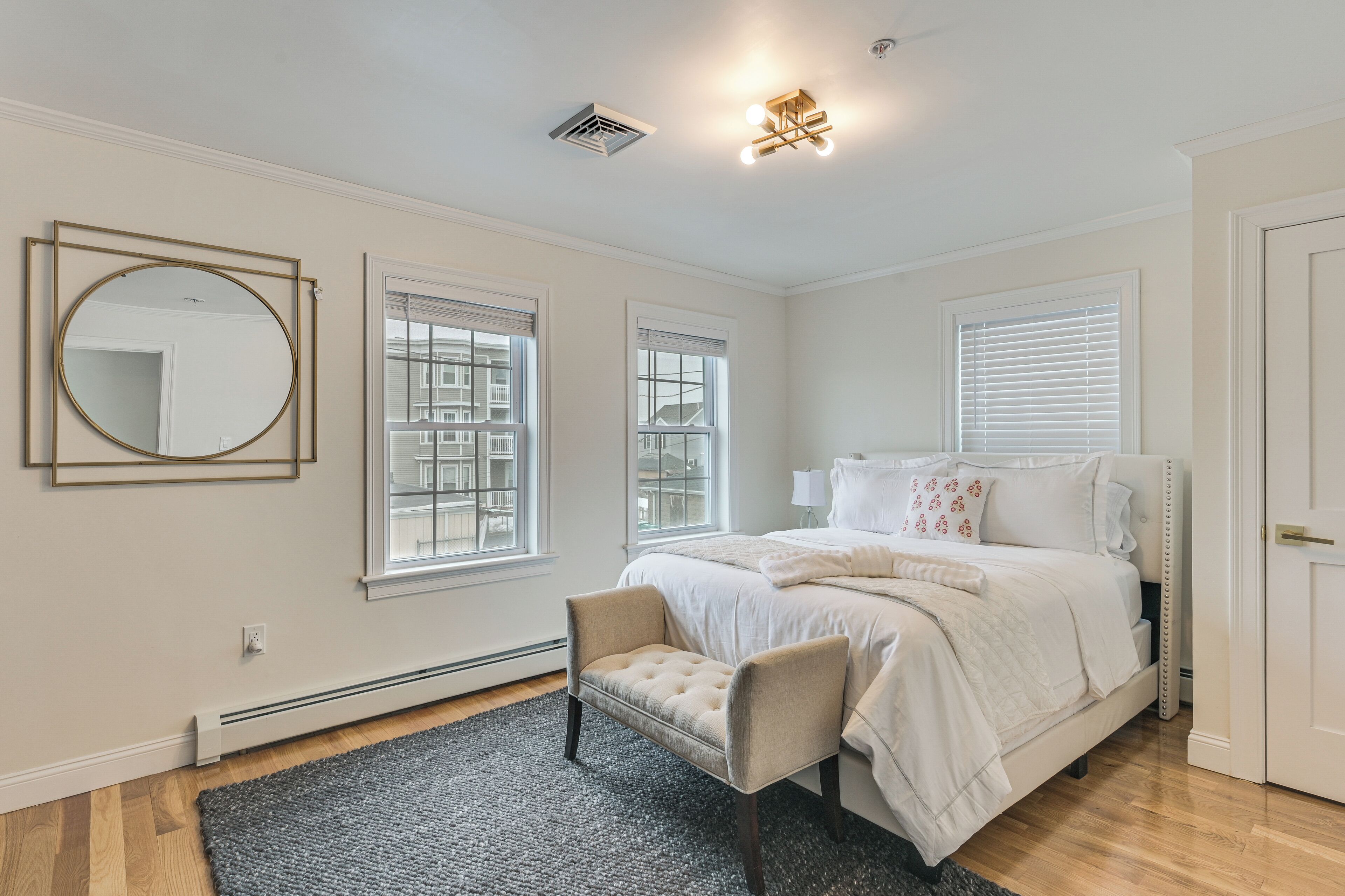 Une chambre à coucher avec un lit, une chaise, un miroir rond et une fenêtre.