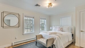 Een slaapkamer met een bed, een stoel, een ronde spiegel en een raam.