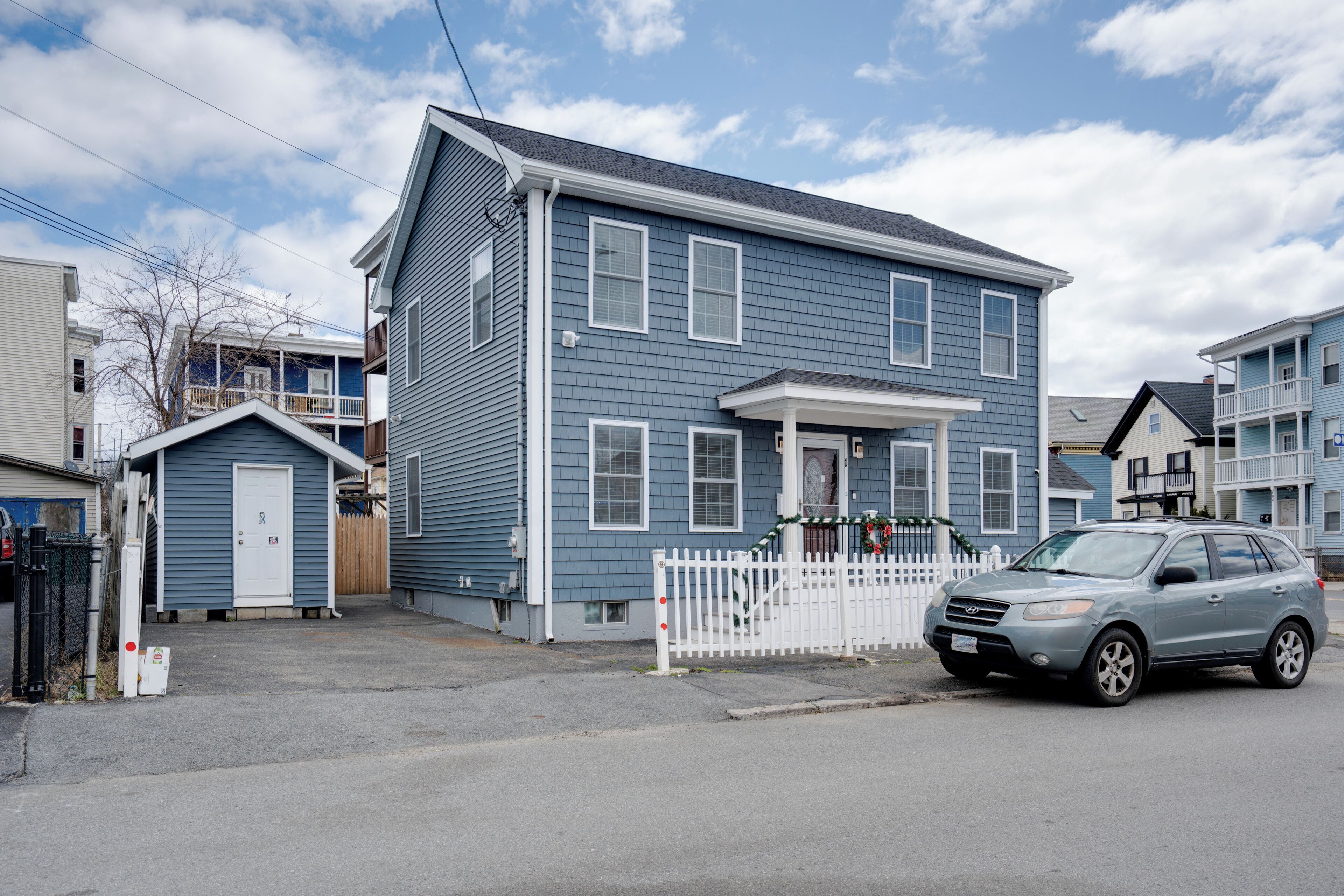 Un immeuble résidentiel de deux étages, doté d’un garage, d’une allée bordée d’une clôture et d’une voiture garée.