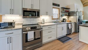 A modern kitchen with white cabinets, stainless steel appliances, and a wooden ceiling. - 2BD Mtn Retreat near Nantahala w/ Firepit and Pond (Andrews)