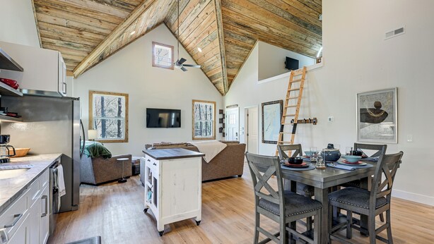 A spacious kitchen with a wooden ceiling, a dining area with a table and chairs, a sofa, and a TV mounted on the wall. - 2BD Mtn Retreat near Nantahala w/ Firepit and Pond (Andrews)