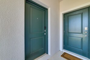 A green door with a doormat and a wall-mounted intercom.