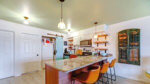 Una cocina con una isla central, taburetes de bar, microondas y refrigerador.