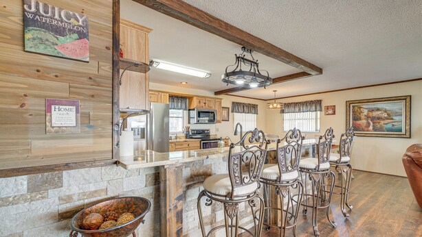 Una cocina con salpicadero de piedra, armarios de madera, una zona de bar con sillas de metal y una mesa de comedor.