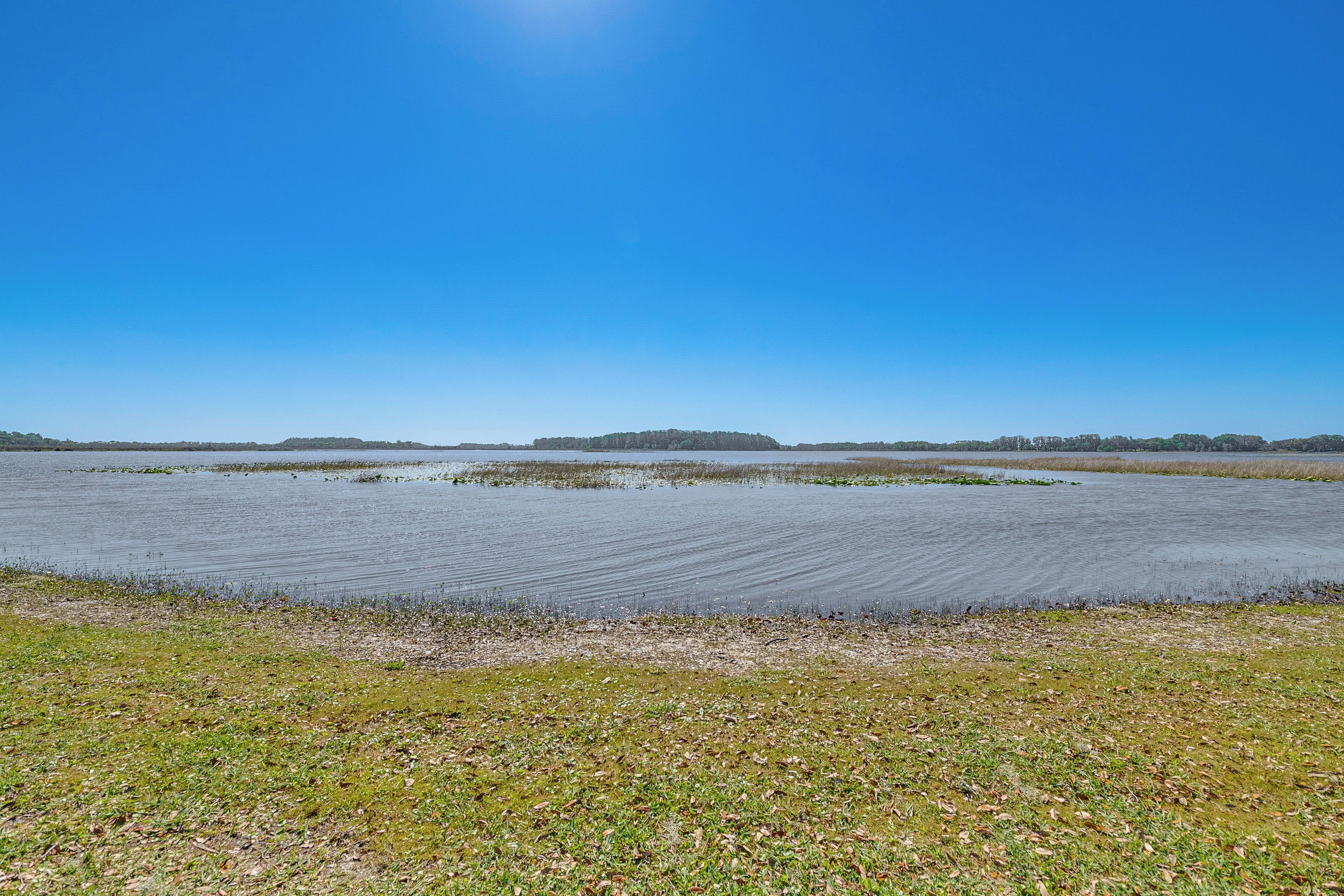 A flat landscape with water and grassy areas under a clear sky.